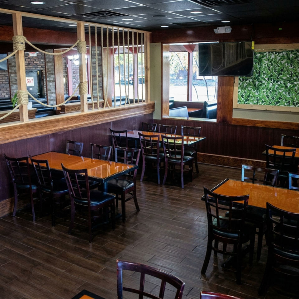 Warmly lit restaurant dining area with wooden tables, black chairs, rope partitions, brick walls, and leafy wall decor.