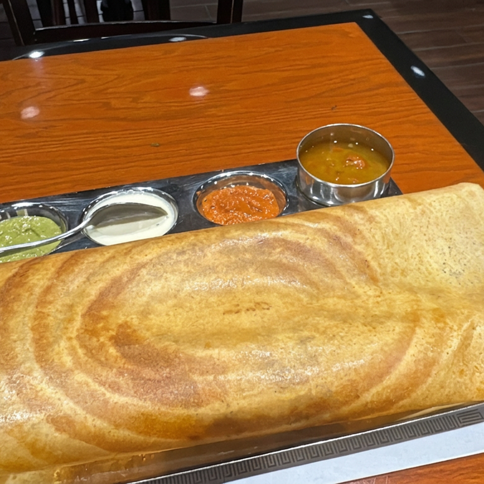 Large golden dosa served on a platter with bowls of coconut chutney, yogurt sauce, tomato chutney, and sambar.